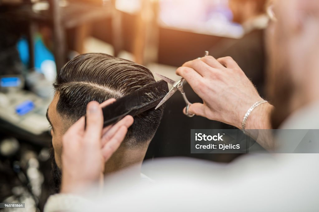 Barber cutting hair with scissors at Maher Cutz