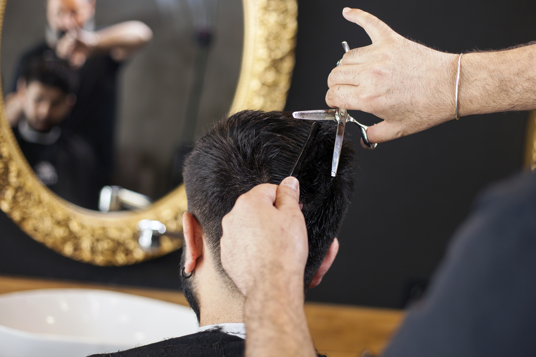 Barber cutting hair with scissors at Maher Cutz